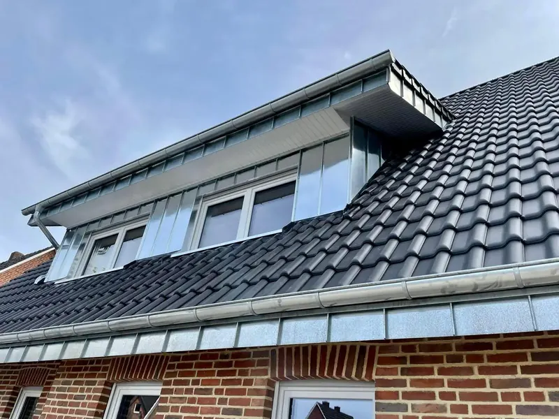 Steildach mit anthrazitfarbenen Pfannen und verkleideter Gaube über Klinkerfassade